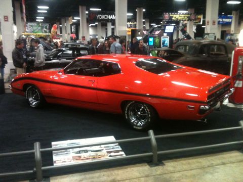 2004 Ford Crown Victoria - A bright red coupe with black racing stripes is displayed indoors, likely at a car show.
