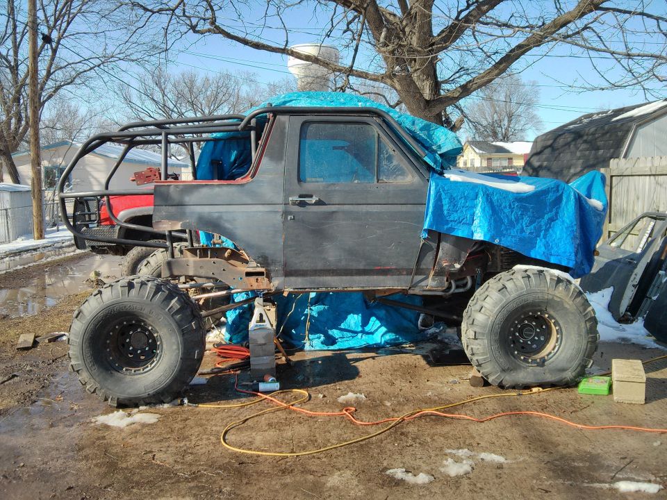 SUV body on a custom frame with large tires, covered in tarps, undergoing modifications