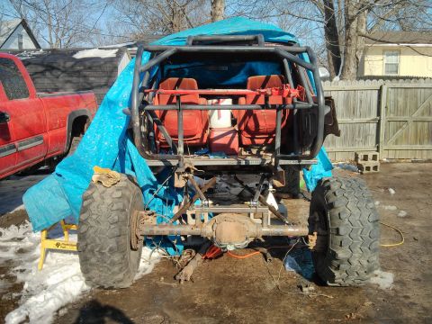 1986 Ford Bronco - Modified off-road vehicle with custom roll cage and large tires, seen next to a red pickup truck.