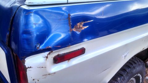 1979 Ford Bronco - The rear corner of a two-tone truck shows significant damage and rust, with a red reflector light visible.