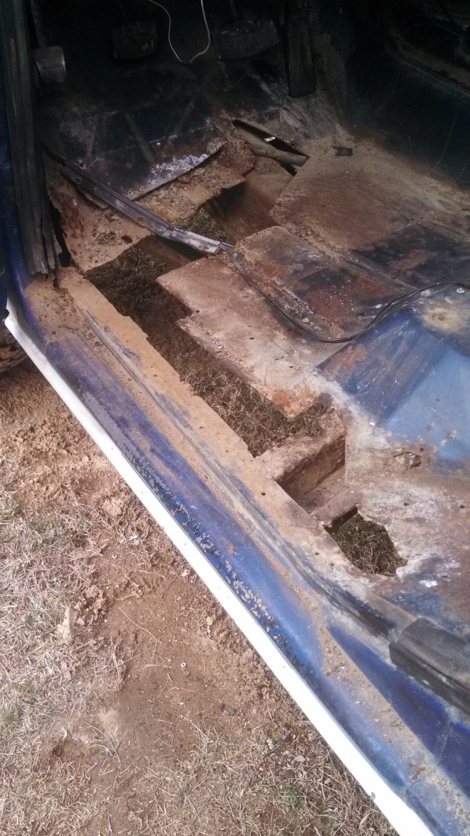 Blue vehicle interior showing severely rusted floor panels and exposed ground beneath