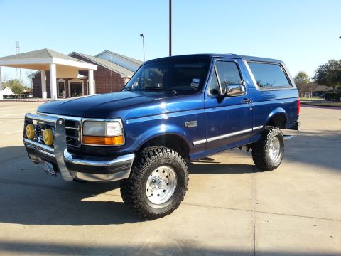 1995 Ford Bronco - This lifted blue 1995 Ford Bronco features a chrome brush guard with auxiliary lights and aggressive off-road tires.