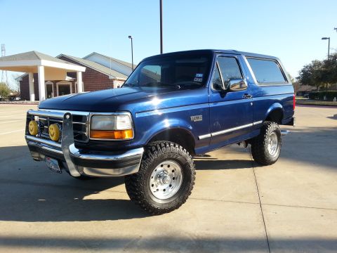 1995 Ford Bronco - This lifted Ford Bronco is parked in a lot with a building in the background.