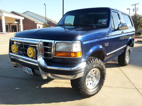 1995 Ford Bronco - This lifted blue Ford Bronco is parked outside a building on a sunny day.