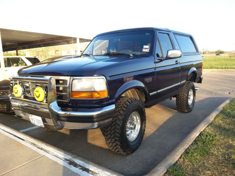 1995 Ford Bronco - A lifted dark blue Ford Bronco is parked outside under a covered area.