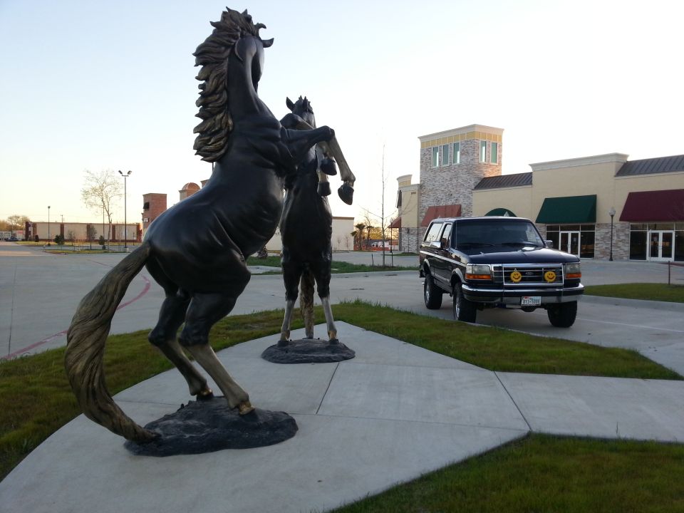 Dark SUV parked on pavement near large horse sculptures in front of a strip mall
