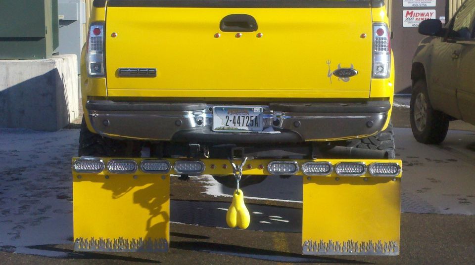 Rear of yellow Ford pickup with custom LED light bar, flame-cut yellow mud flaps, and Montana plate