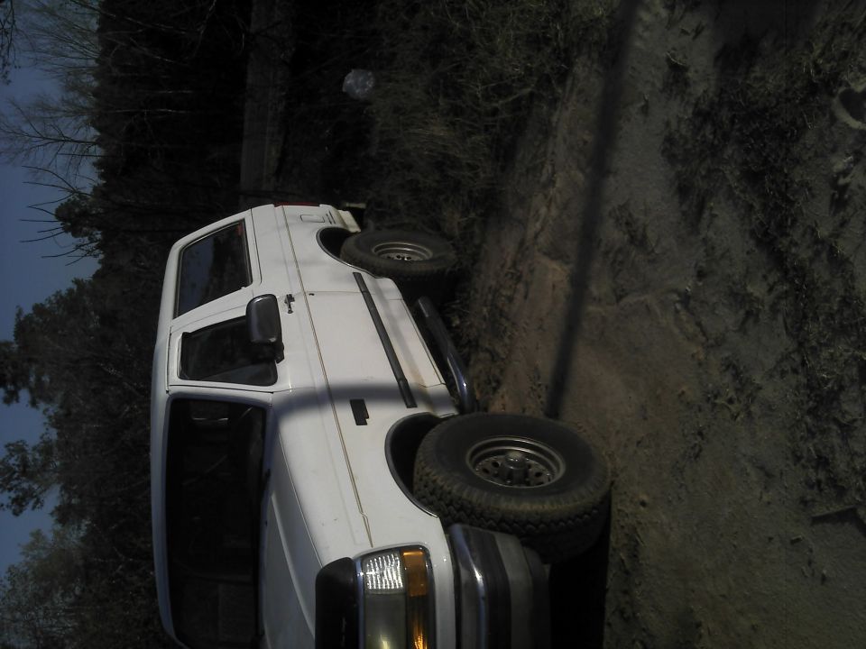 White van parked on a dirt incline with trees in the background