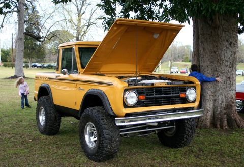 1980 Ford Mustang - A yellow 1977 Ford Bronco is parked on grass with its hood open, revealing the engine bay.