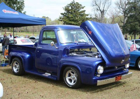 1980 Ford Mustang - A classic blue Ford F-100 pickup truck is displayed with its hood open at an outdoor event.