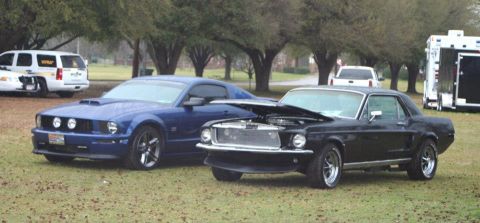 1980 Ford Mustang - A classic black 1968 Ford Mustang coupe sits with its hood open, parked beside a blue modern Mustang.