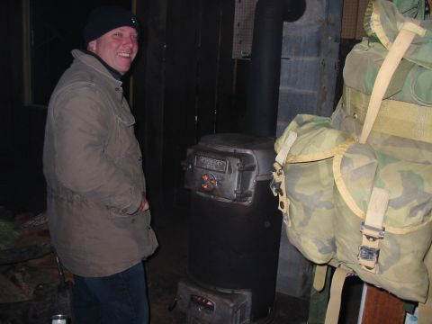 1992 Ford Bronco - A man smiles while standing next to a wood-burning stove, with a camouflage backpack to his right.