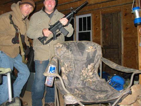 1992 Ford Bronco - Two men pose with firearms inside a rustic wooden building, a camouflage chair and beverages nearby.
