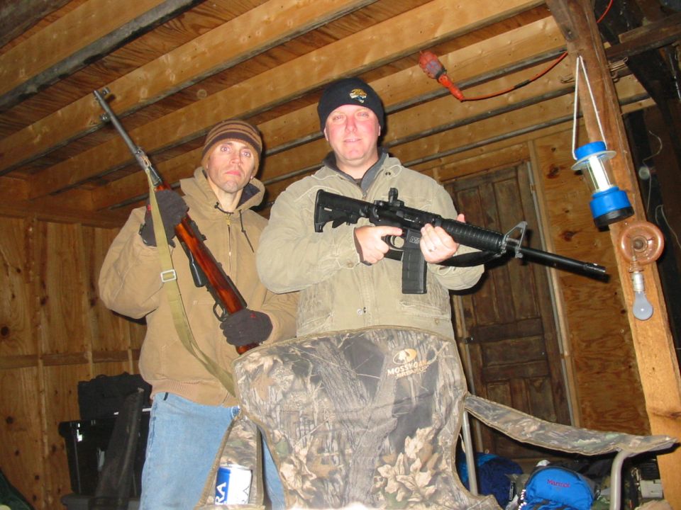Two men holding rifles inside a wooden structure