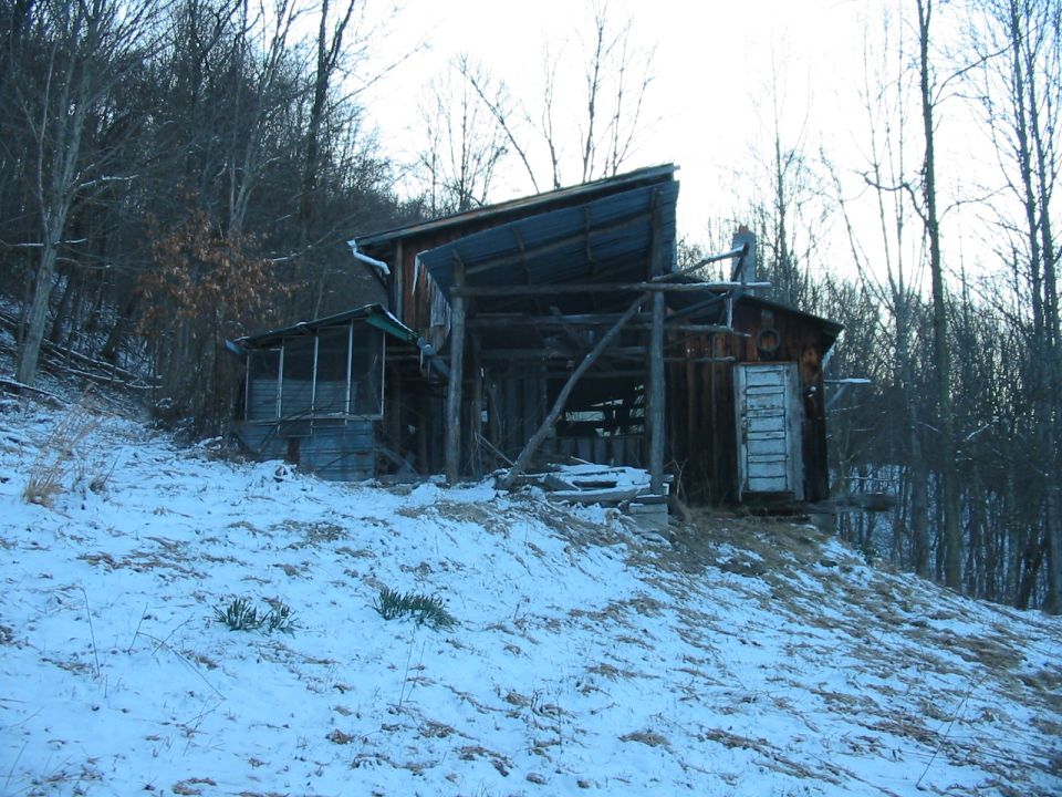 Dilapidated wooden barn with a metal roof, set on a snowy hillside