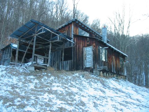 1992 Ford Bronco - An old, weathered wooden cabin sits on a snowy hillside under a gray sky, with an attached open-air structure.