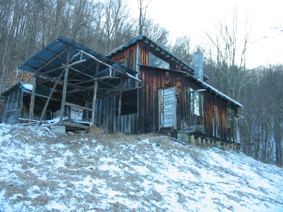 Dilapidated wooden cabin with snow and bare trees