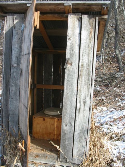 1992 Ford Bronco - An old wooden outhouse stands in a snowy, wooded area.