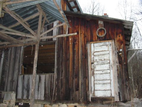 1992 Ford Bronco - A weathered wooden structure with a corrugated metal roof extension and a distressed white door stands in an outdoor setting.