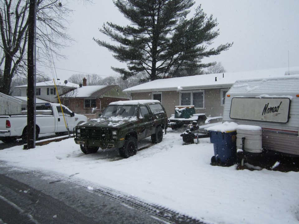 Dark green SUV parked in snow next to a white pickup truck and a trailer