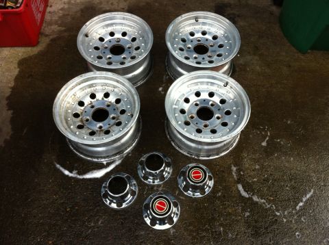 1992 Ford F-150 - Four aluminum wheels and hubcaps are laid out on a wet surface, possibly after cleaning.