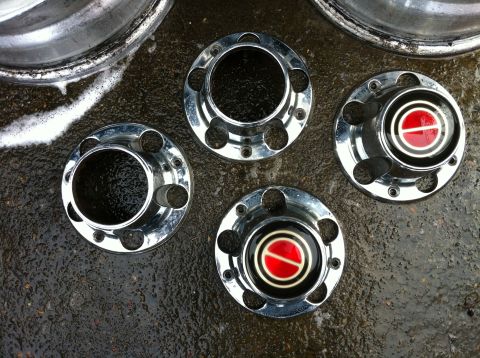 1992 Ford F-150 - Four chrome hubcaps, two with red and white emblems, are laid out on wet asphalt.