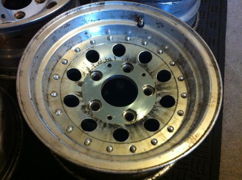 1992 Ford F-150 - Close-up of a polished aluminum eight-lug wheel lying face-up on a rubber mat, showing its simulated beadlock bolt ring, twelve round vent…