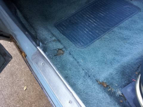 2008 Subaru Legacy - The interior shows worn blue carpeting with a rubber floor mat and visible damage to the carpet.