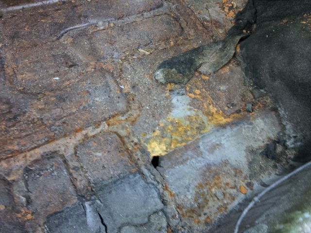 Close-up of a heavily rusted and corroded car floor pan with a dark, possibly rubberized, material attached