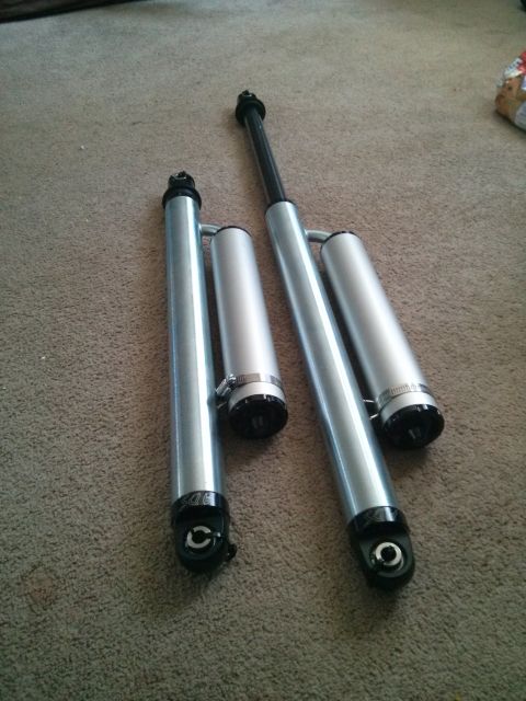 1986 Ford Bronco - Two silver shock absorbers are laid out on a carpeted surface.