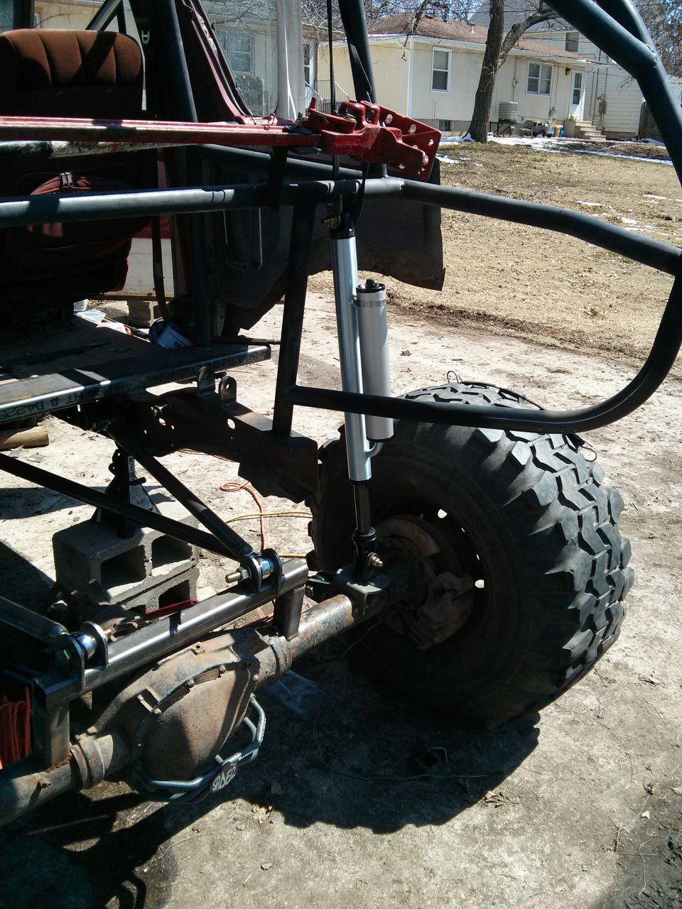 Modified off-road vehicle chassis with large tire, suspension, and roll cage. Red jack visible