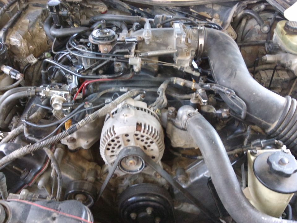 Engine bay with alternator, hoses, and intake manifold visible. Watermark says SUPERMOTORS.NET