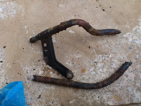 1998 Ford Crown Victoria - A heavily rusted metal pipe part lies on a concrete surface, likely removed from a vehicle.