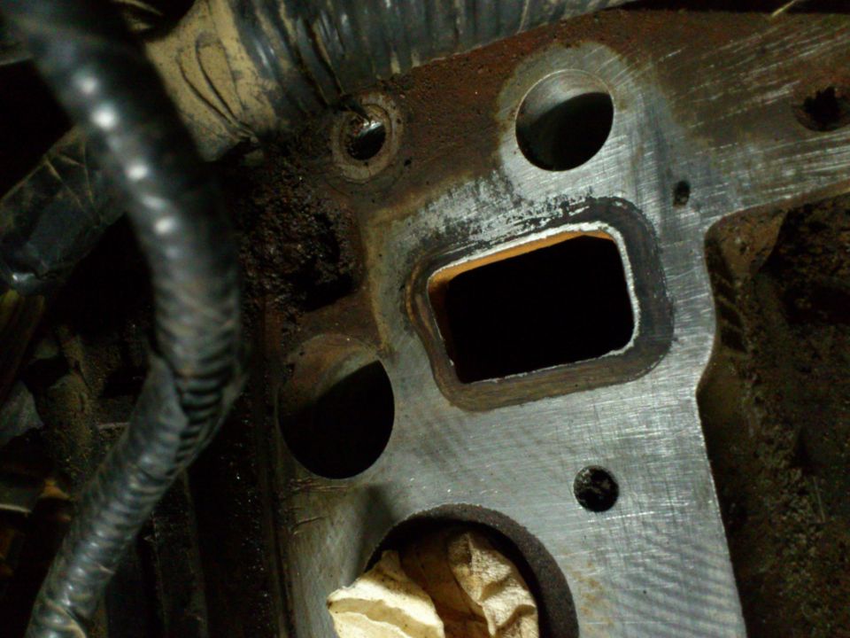 Close-up of an engine intake manifold with a rectangular opening and bolt holes