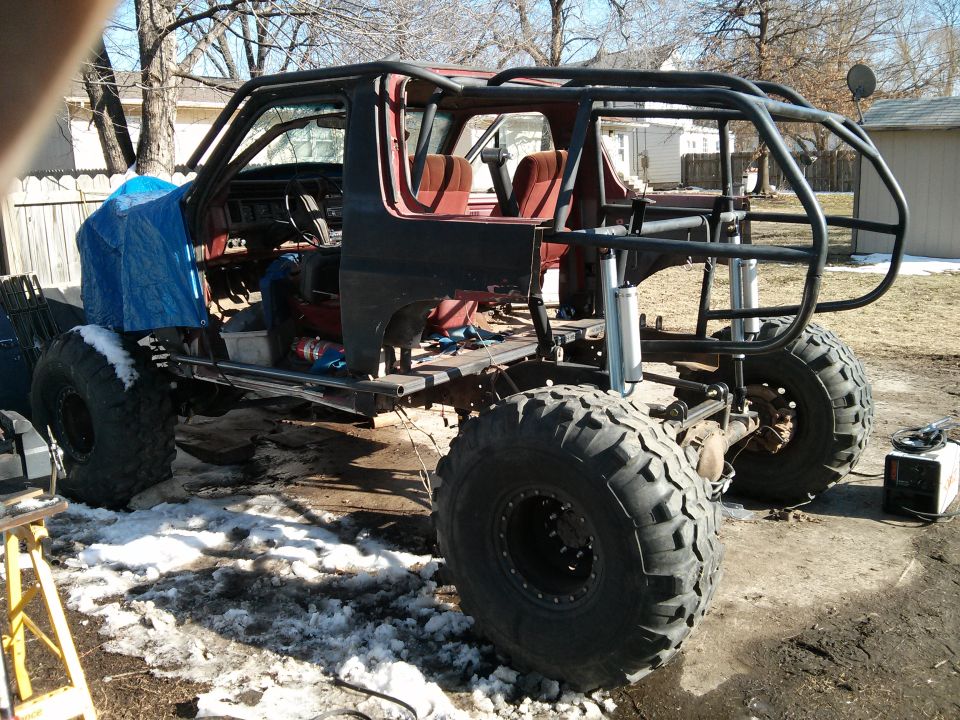 1986 Ford Bronco modified with a roll cage and large off-road tires, undergoing construction