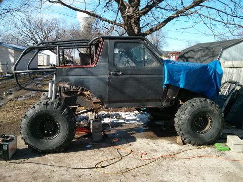 1986 Ford Bronco - This heavily modified SUV is undergoing custom work, a prominent roll cage and oversized tires.