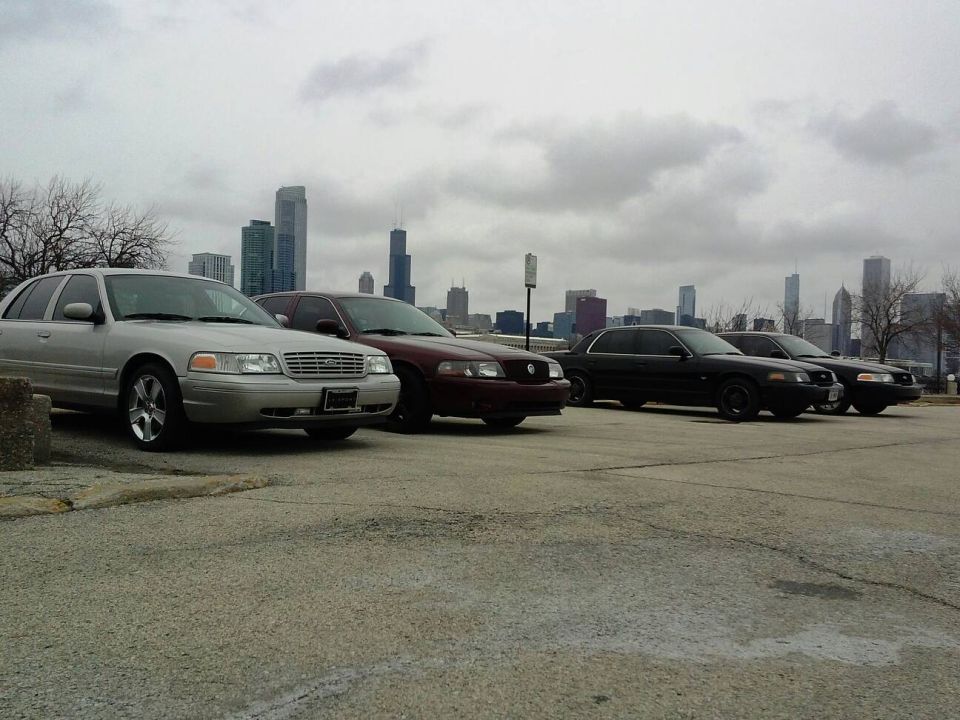Silver 2003 Ford Crown Victoria parked in front of a city skyline