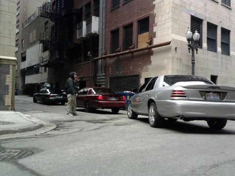 2003 Ford Crown Victoria - Rear view of a silver 2003 Ford Crown Victoria parked in an urban alleyway with other vehicles present.