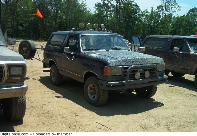 Dark blue Ford Bronco with roof light bar and brush guard, muddy, on a dirt lot