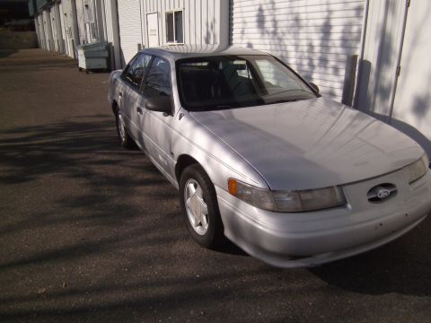 1992 Ford Taurus - A silver 1992 Ford Taurus is parked in front of a commercial building with white siding.