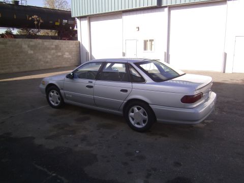 1992 Ford Taurus - This silver 1992 Ford Taurus sedan is shown from the rear three-quarter angle, parked outdoors near a building and train cars.
