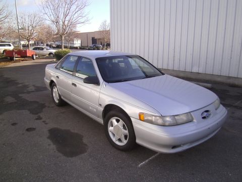 1992 Ford Taurus - This silver sedan is parked in front of a corrugated metal building on a cloudy day.