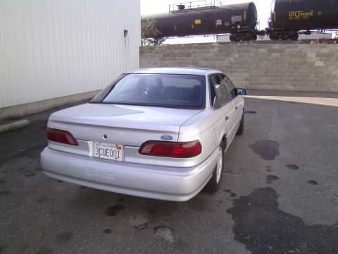 1992 Ford Taurus - Rear view of a 1992 Ford Taurus sedan parked on asphalt near a building and train cars.