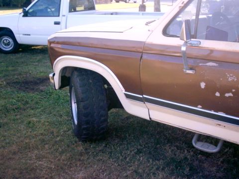 1980 Ford Bronco - Close side view of the front fender and passenger door on a two-tone brown and cream 1980s Ford truck parked on grass, showing peeling pain…