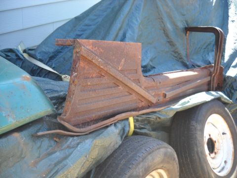 1954 Ford F-100 - Rusted truck bed part covered by a tarp, with tires visible underneath.
