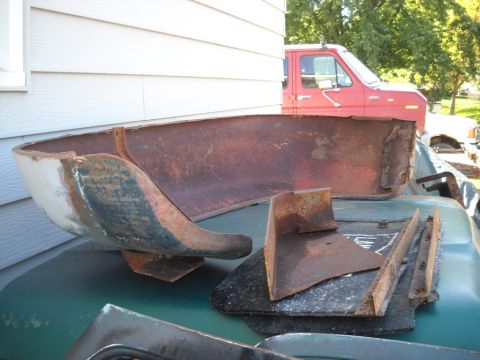 1954 Ford F-100 - Several rusty metal truck bed sections and brackets are laid out on a green surface, with a red truck visible behind them.
