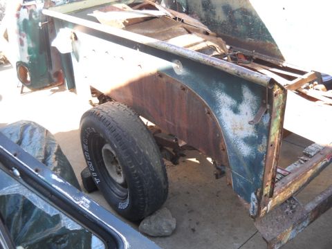 1954 Ford F-100 - A partially dismantled truck bed and fender, showing its weathered green paint and a single tire.