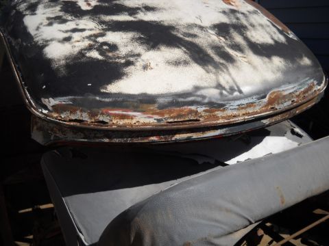 1954 Ford F-100 - Close-up of a heavily rusted car hood and a gray seat, likely from a donor vehicle.