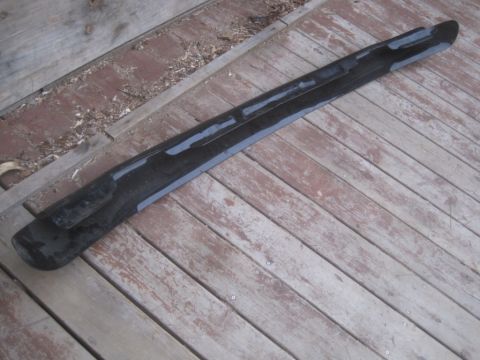 1993 Ford Bronco - A black plastic trim piece, likely for a vehicle, lies on weathered wooden planks.