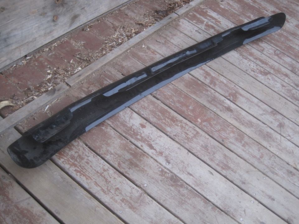 Black plastic trim piece with gray adhesive strips on wooden planks
